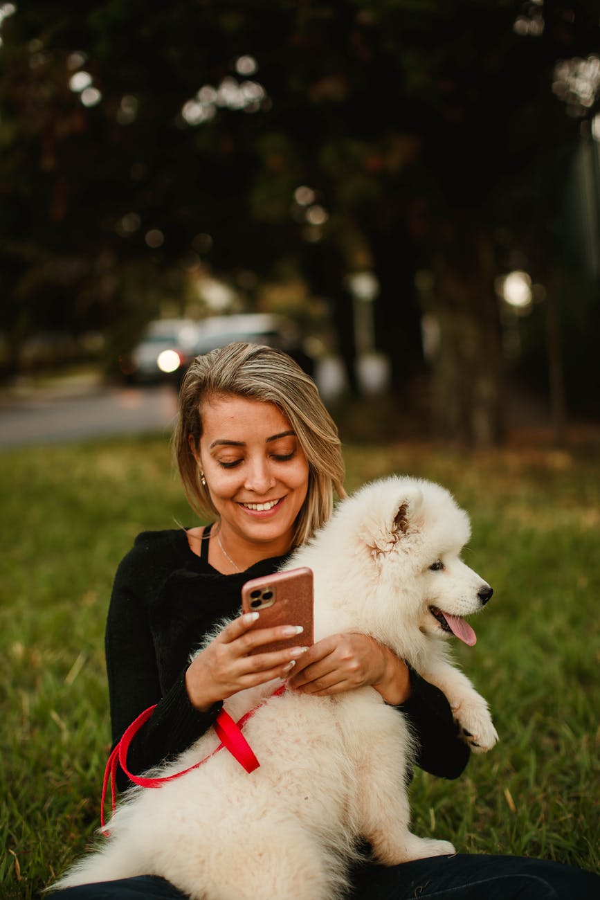 smiling woman with dog using smartphone in park